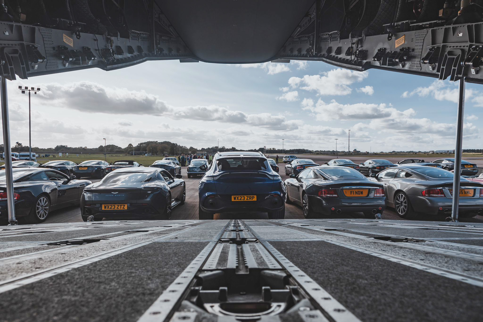 Photo - Aston Martin vehicles lined-up behind an Atlas C Mk.1 (A400M), viewed from the aircraft ramp